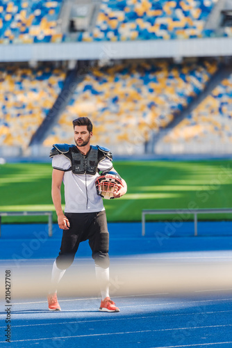 handsome young american football player standing alone at sports stadium