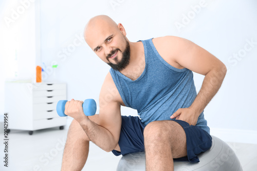 Overweight man doing exercise with dumbbell in gym © New Africa