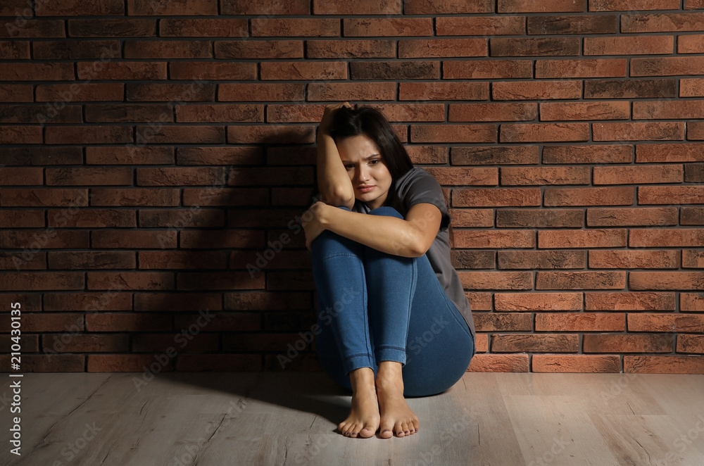 Depressed young woman sitting on floor near brick wall Depressed young woman sitting on floor near brick wall