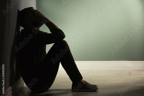 Depressed young man sitting on floor in darkness photo