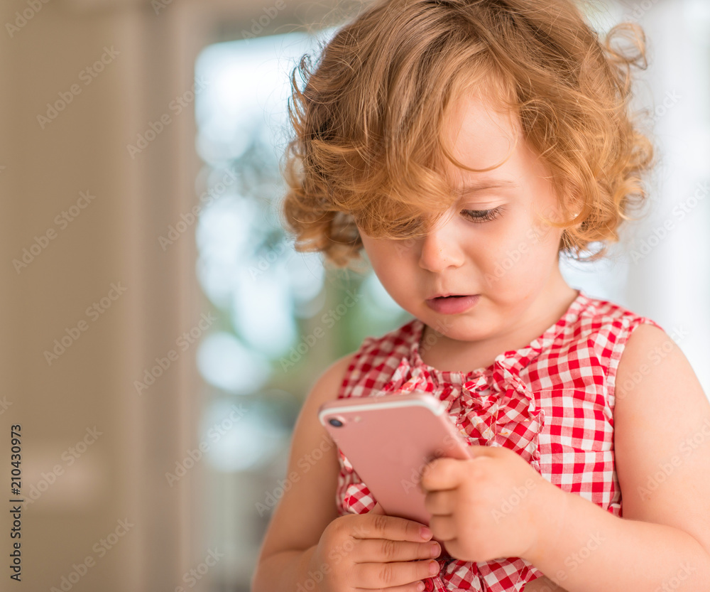 Beautiful blonde child holding and looking at smartphone at home. Beautiful blonde child holding and looking at smartphone at home.