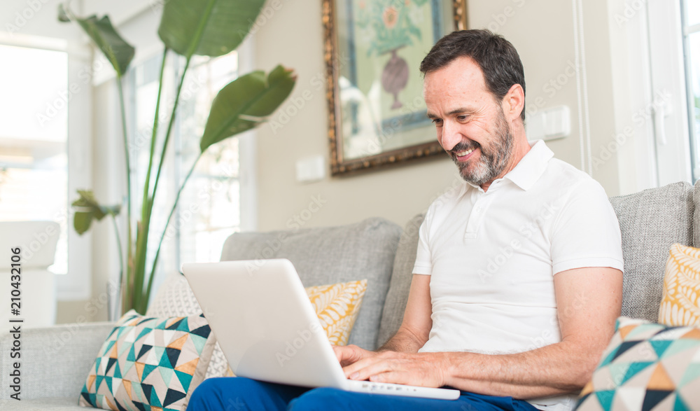 Middle age man using laptop at sofa with a happy face standing and smiling with a confident smile showing teeth Middle age man using laptop at sofa with a happy face standing and smiling with a confident smile showing teeth