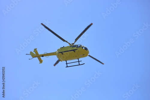 Fototapeta Naklejka Na Ścianę i Meble -  Żółty helikopter w powietrzu w trakcie lotu, widok z dołu, z ziemi