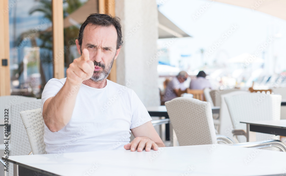 Handsome senior man sitting at terrace pointing with finger to the camera and to you, hand sign, positive and confident gesture from the front Handsome senior man sitting at terrace pointing with finger to the camera and to you, hand sign, positive and confident gesture from the front