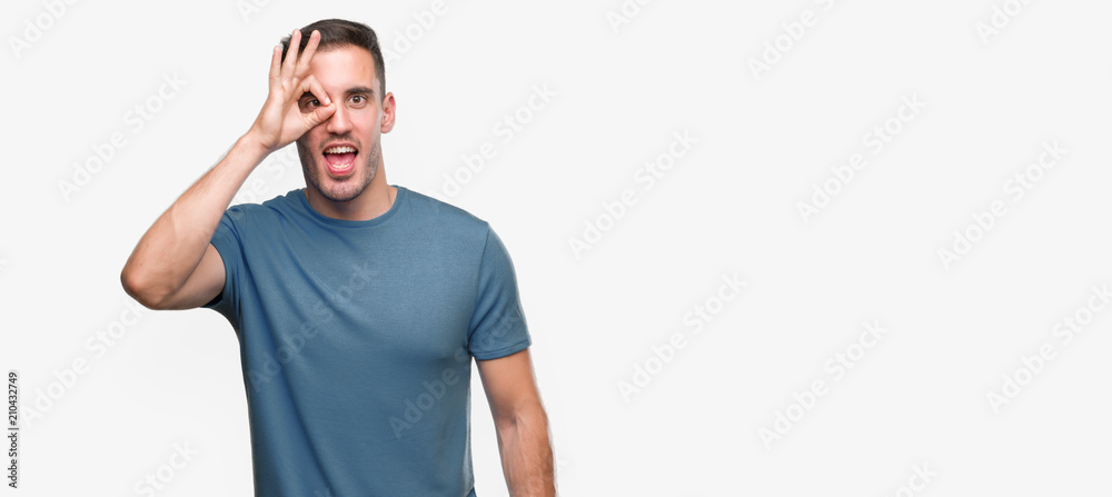 Fototapeta premium Handsome young casual man doing ok gesture with hand smiling, eye looking through fingers with happy face.