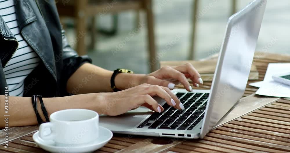 Tracking shot of unrecognizable young woman working online with laptop computer at table in open air cafe, close up of hands