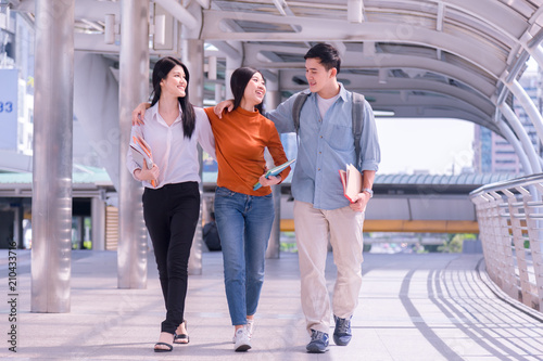 Front view of three asian students walking and talking in an university campus.