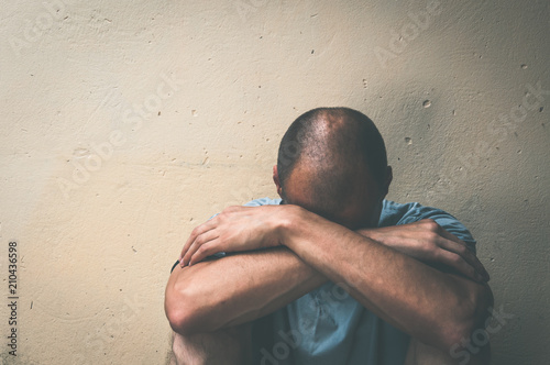 Homeless man drug and alcohol addict sitting alone and depressed on the street in the shadow feeling anxious and lonely, social documentary concept