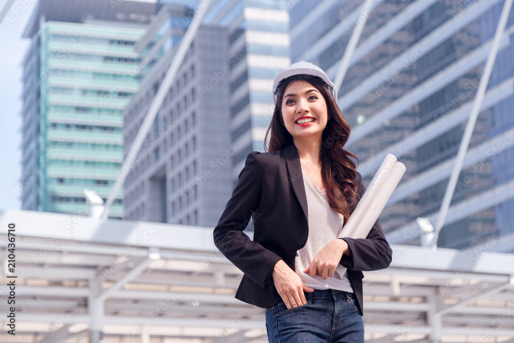 Portrait of Happy professional construction engineer woman holding the blueprint and wearing the safety helmet and glasses at the building site place background,