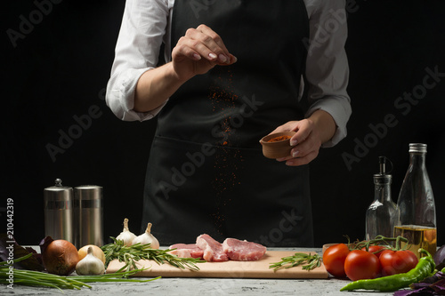 Steak for grilling for chefs. Preparation of fresh beef or pork. Strewing paprika or red pepper. Horizontal photo with dark black background. photo