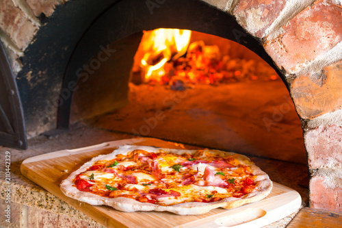 Rustic home-made pizza prosciutto baked in a wood fired brick oven with fire ...
