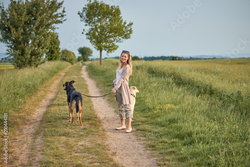 Hübsche junge Frau steht mit ihren Hunden auf einem Feldweg