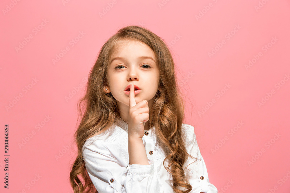 The young teen girl whispering a secret behind her hand over pink background The young teen girl whispering a secret behind her hand over pink background