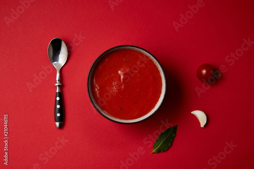 top view of tasty tomato soup in plate, spoon, fresh tomato and garlic on red table © LIGHTFIELD STUDIOS