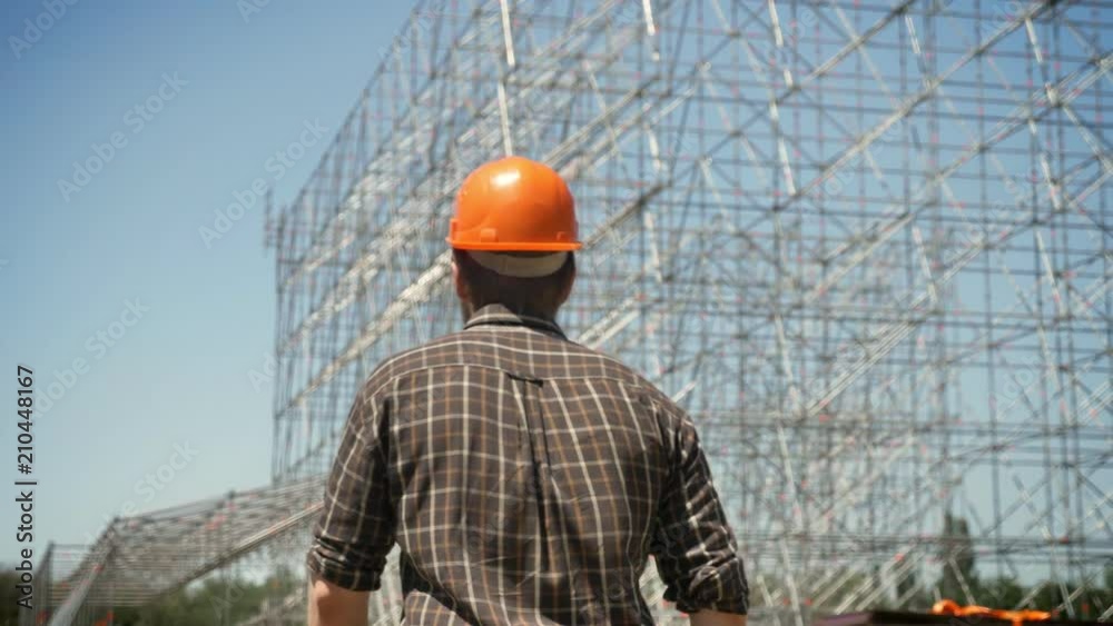 Back of male architect in helmet walking toward metal installation on background Back of male architect in helmet walking toward metal installation on background