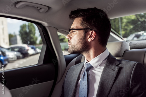 portrait of pensive businessman in eyeglasses looking out car window while sitting on backseat in car © LIGHTFIELD STUDIOS