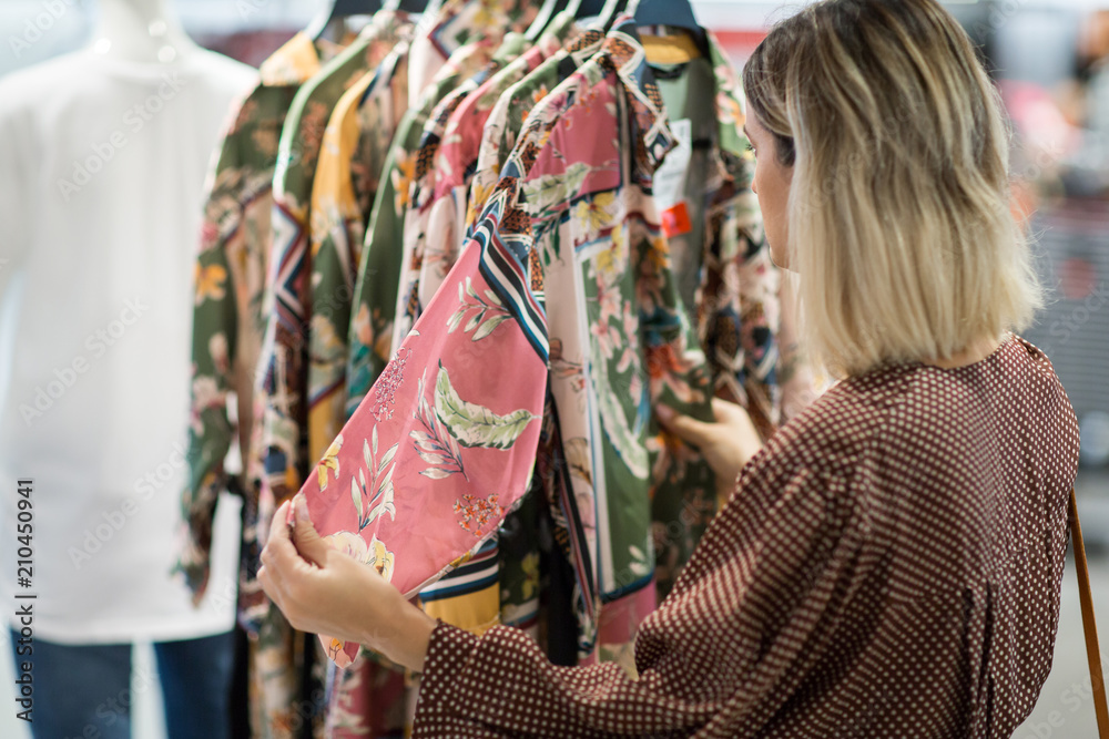Young woman choosing clothes in mall or clothing store - Shopping, fashion, style and people concept Young woman choosing clothes in mall or clothing store - Shopping, fashion, style and people concept