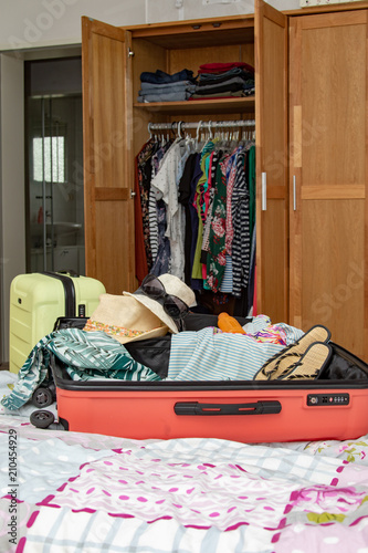 Verschiedene Kleidungsstücke für den Sommer auf Koffern vor geöffnetem Kleiderschrank