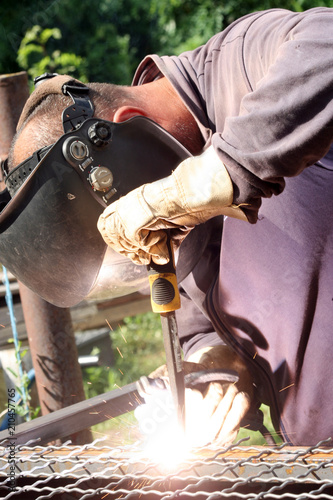 Welder welding a metal part wearing standard protection equipment