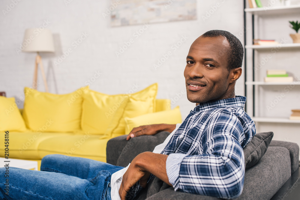 handsome young african american man sitting in couch and smiling at camera