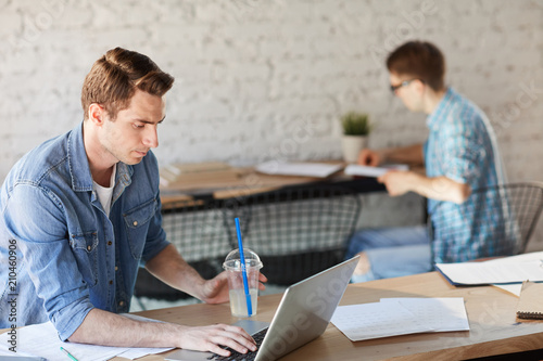 Young architect or designer with drink networking in front of laptop and searching for new ideas