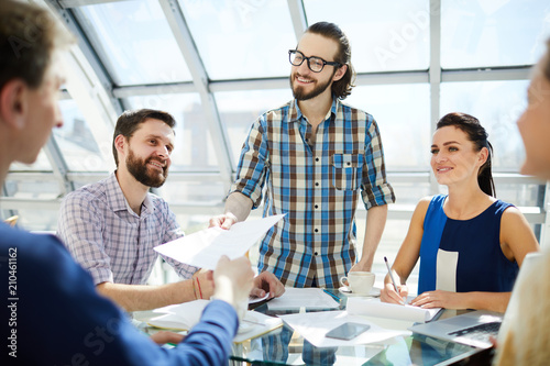 Happy young businessman passing over financial document to colleague to read or sign