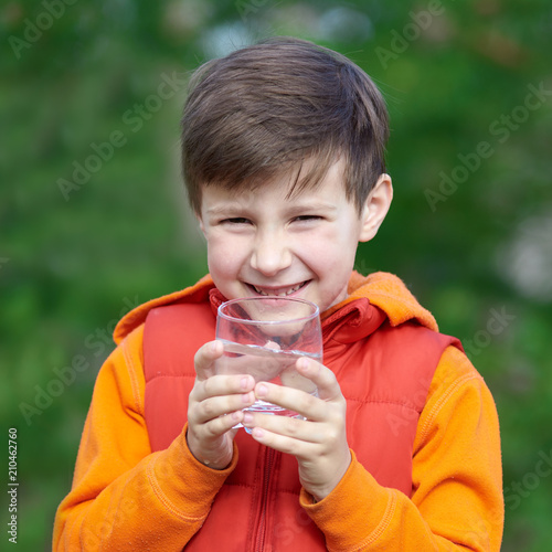 Outdoor portrait of smiling European boy with a glass of water.