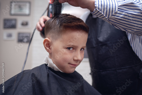 Cheerful Caucasian boy  getting hairstyle in barbershop.