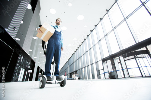 Young worker of delivery service in uniform moving on hoverboard while getting parcel to client photo