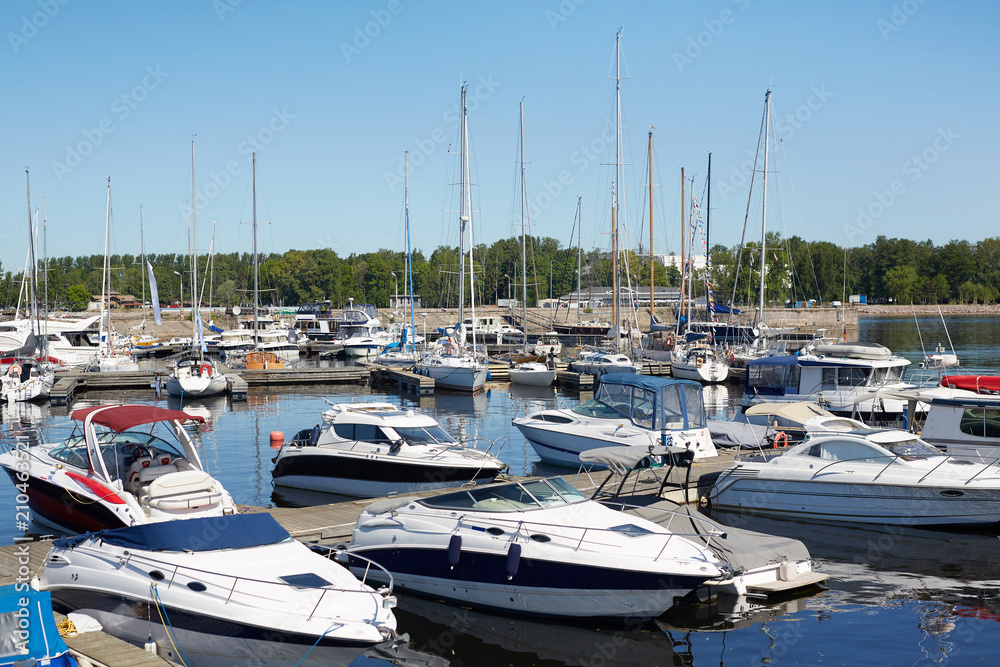 Group of yachts on water on hot summer day with blue sky above and green trees on horizon