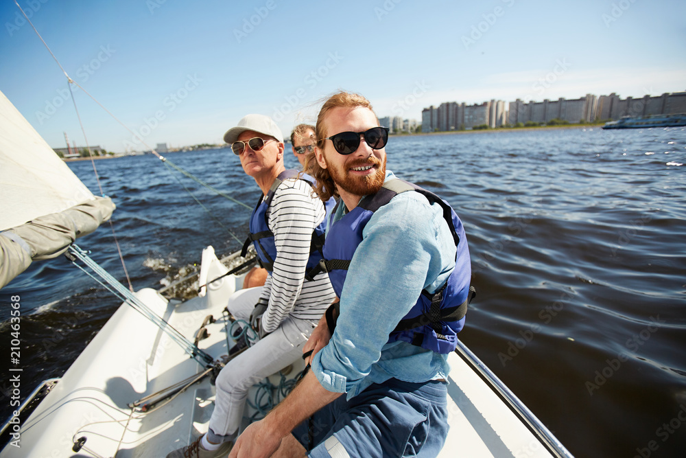 Fototapeta premium Active men in sunglasses sitting on yacht while floating in lake on hot summer day