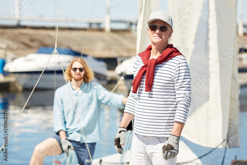 Senior man and his assistant in sunglasses working on yacht while preparing for new sailing season