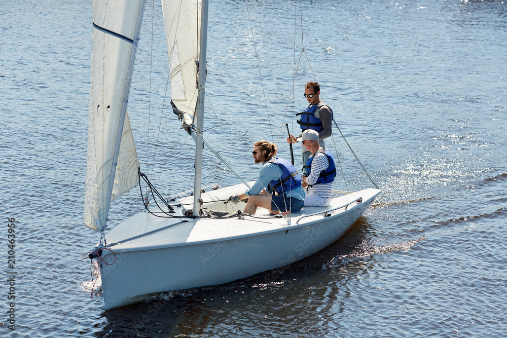 Fototapeta premium Three men in lifejackets sitting in yacht and sailing in the sea during weekend trip