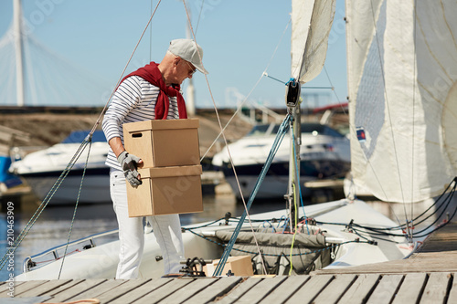 Senior man in casualwear carrying packed boxes while working on his yacht on summer day