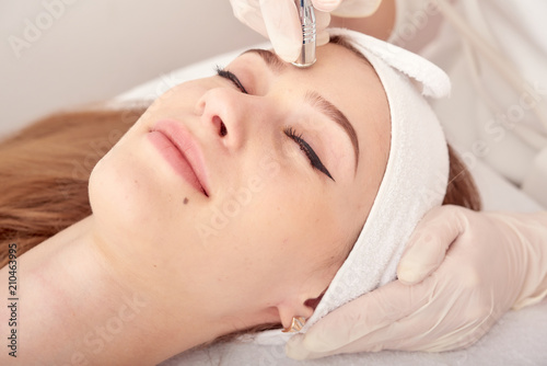 The cosmetologist makes the procedure Microdermabrasion of the facial skin of a beautiful, young woman in a beauty salon.Cosmetology and professional skin care. photo