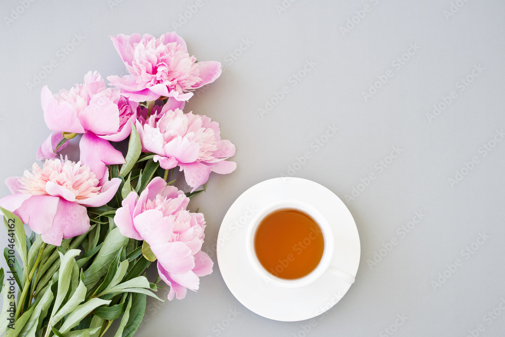 Cup of tea, a saucer and a bouquet of pink peonies on a gray surface, top view