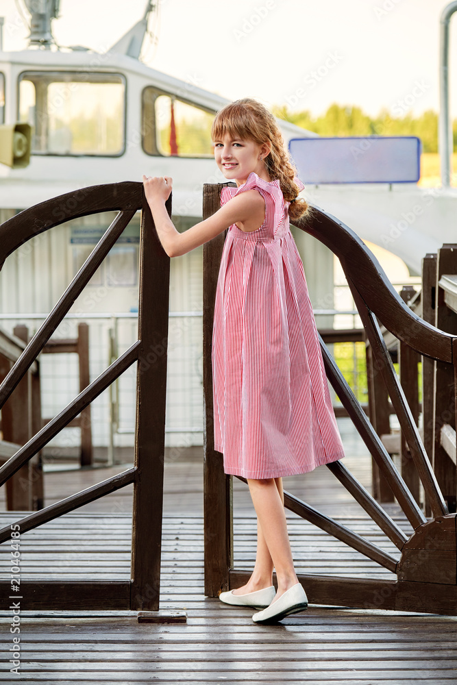 Young lady child 11 years old is standing near a wooden bridge, looking  camera, outdoors.Full