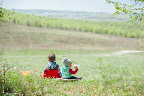 Little boy and baby girl sitting on a background of green landscape. photo