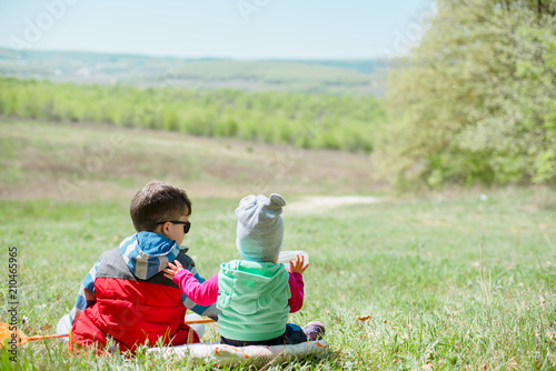Little boy and baby girl sitting on a background of green landscape. photo