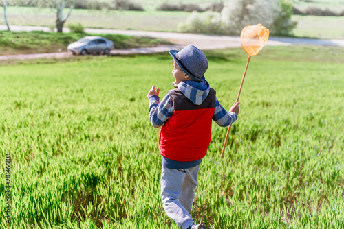 Little boy with a butterfly net in hand runs across the green field. photo