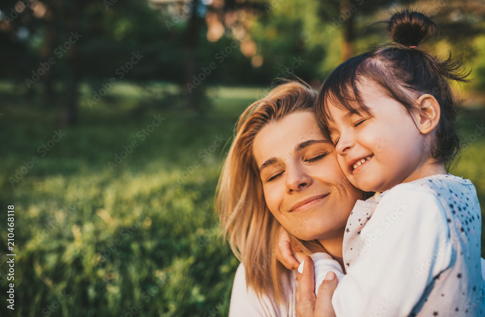 Close up portrait of beautiful happy girl kid embrace her mother outdoor on green grass. Beautiful woman and her cute child enjoy time together in the park. Happy Mother's Day. Motherhood, childhood Close up portrait of beautiful happy girl kid embrace her mother outdoor on green grass. Beautiful woman and her cute child enjoy time together in the park. Happy Mother's Day. Motherhood, childhood