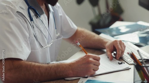 Caucasian doctor with stethoscope on neck sitting at table in doctor’s office, shaking patient’s hand. Indoors. Popular clinic of the city.