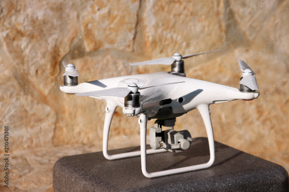 White quadcopter Drone with 4K digital camera on stand is ready for take off to fly in air to take photos, record footage from above. Drone with four motors, propellers, camera and red warning lights.