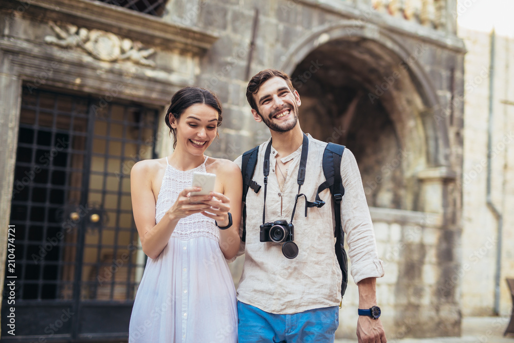 Naklejka premium Traveling couple of tourists walking around old town, and using smart phone. Vacation, summer, holiday, tourism: concept.