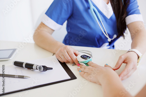 Female doctor with otoscope and pulse oximeter in blue uniform making oxygen test to a patient. Medicine and health care concept. photo
