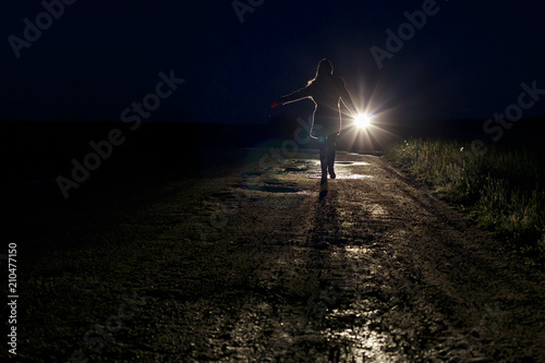 running scared woman at night in the headlights of a car on a country road silhouette