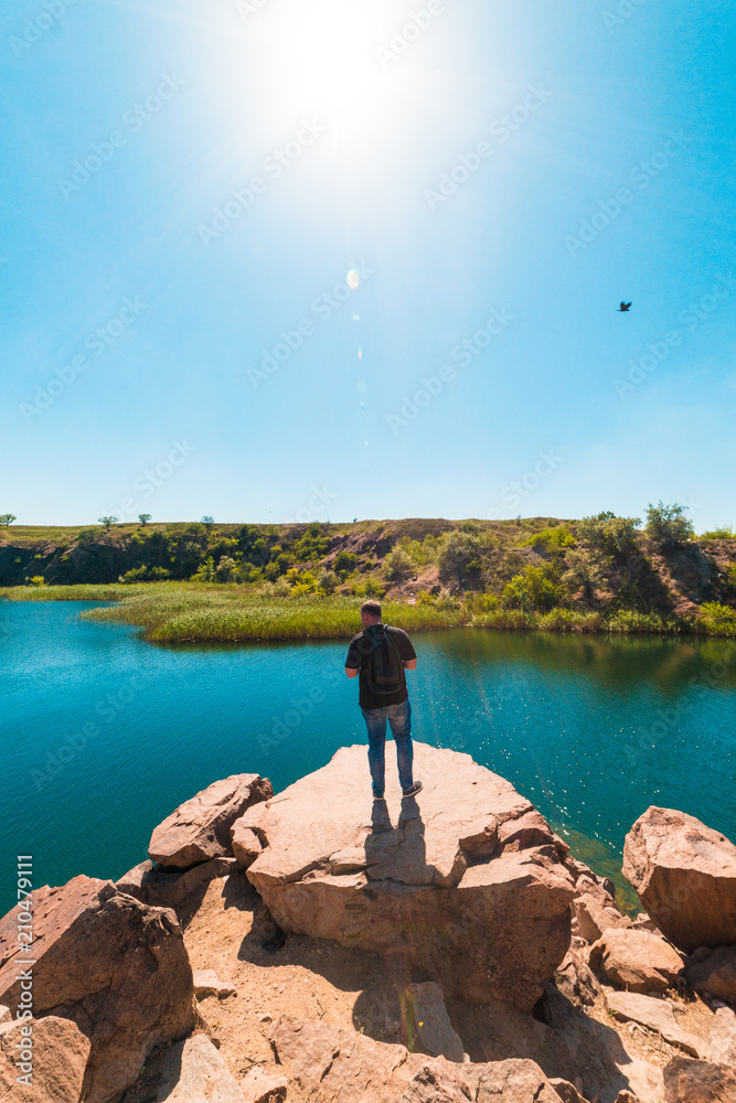 Fototapeta premium guy tourist on a cliff face looking at a pond, tourism, vacation, travel, summer vacation