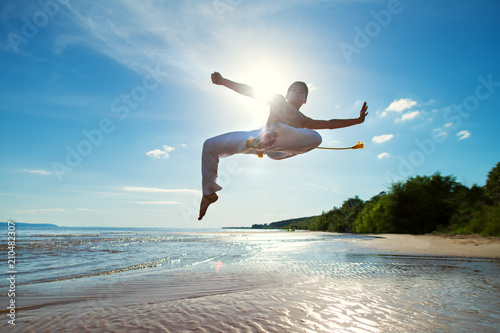 A young guy trains capoeira on the beach.