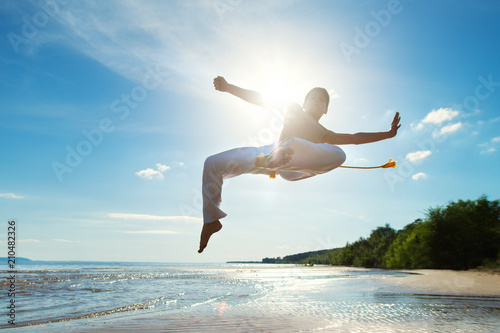 A young guy trains capoeira on the beach.