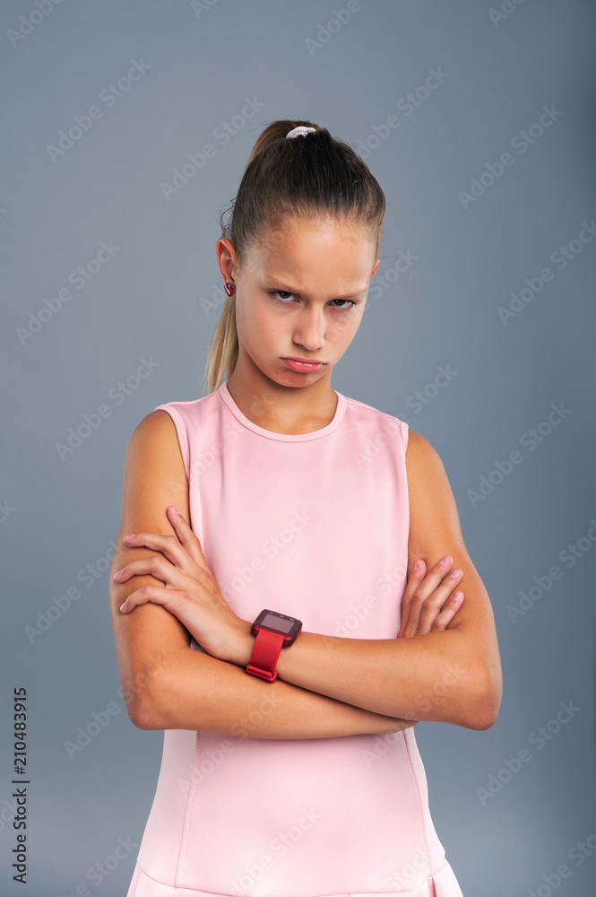 Angry with you. Adorable teenage girl crossing her arms across her chest and glaring while posing isolated on a blue-grey background Angry with you. Adorable teenage girl crossing her arms across her chest and glaring while posing isolated on a blue-grey background